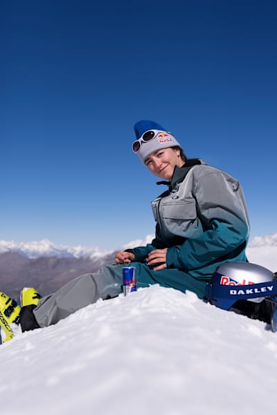 At the 2025 Red Bull Performance Camp in Saas-Fee, Switzerland, Mathilde Gremaud relaxes on snowy slopes with Red Bull and Oakley gear under blue skies.