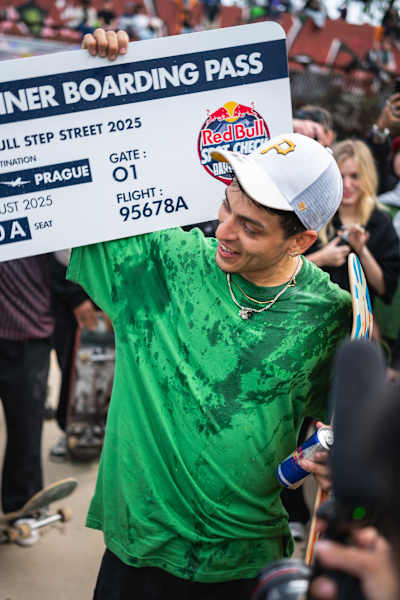 Un momento triunfal cuando el ganador del Red Bull Spot Check 2025 en Barcelona posa con su tarjeta de embarque premiada en un animado ambiente de evento