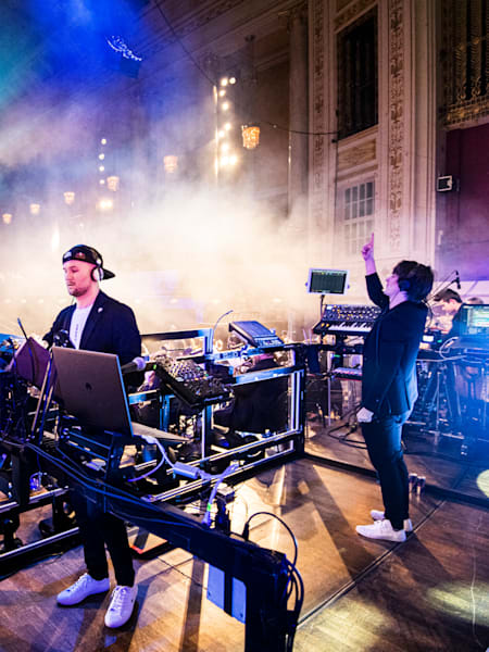 A photo of Austrian electronic music duo Camo & Krooked performing their Red Bull Symphonic Concert with conductor Christian Kolonovits at the Konzerthaus in Vienna, Austria.