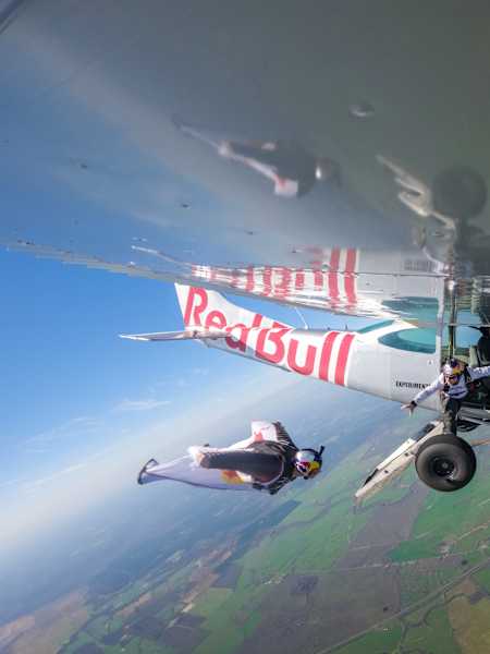 Mike Swanson flies in a wingsuit next to the Plane Swap plane (flown by Luke Aikins) with Jon Devore leaning out to grab a can of Red Bull at the Red Bull Aviation Camp.