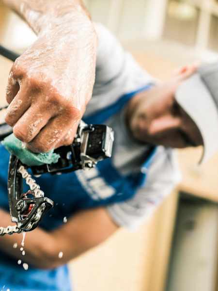 A mechanic cleans the rear derailleur on a bicycle.