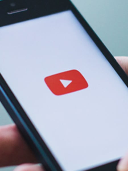 Homem segurando um celular, na tela está aberto o aplicativo YouTube