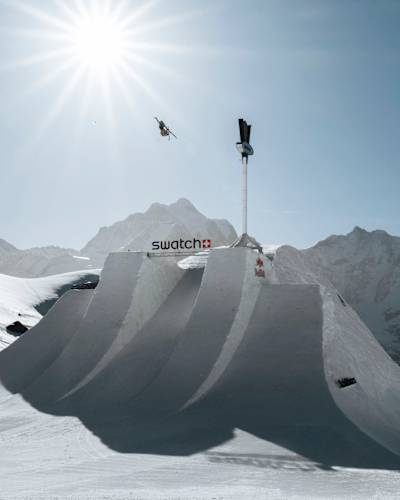 A thrilling ski performance by Finley Melville Ives captured mid-air at Swatch Nines 2024, Schilthorn, Switzerland, set against stunning snow-covered alpine peaks and bright sunlight