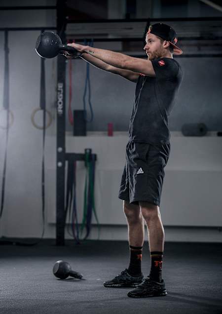 Een sporter voert een kettlebell swing oefening uit tijdens een gymsessie.