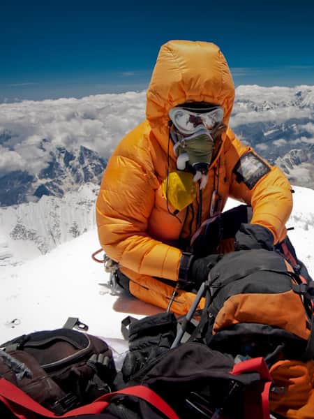 Climber with oxygen mask sorts kit out during an Everest climb.