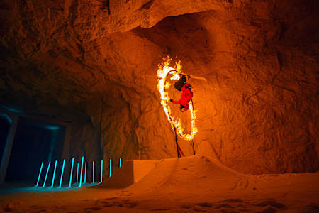 Jesper Tjäder springt in einer Höhle mit seinen Skiern durch einen Ring aus Feuer.