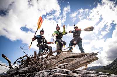 Eric Boomer, Ben Stooksberry and Nouria Newman stand on driftwood with their kayak paddles.