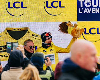 Lorenzo Finn, riding for Red Bull Bora Hansgrohe Rookies, wearing the yellow jersey alongside Bernard Hinault at the finish of the 2026 Tour de l’Avenir.