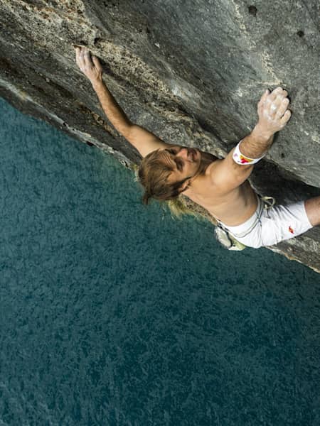 Un escalador intenta subir, sin cuerda, con el agua al fondo que actúa como red de seguridad en caso de caída.