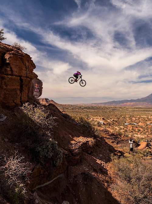 Chelsea Kimball soars off a cliff edge on her mountain bike during the women's final at the extreme Red Bull Rampage freeride event in the rugged Utah desert landscape, 2024