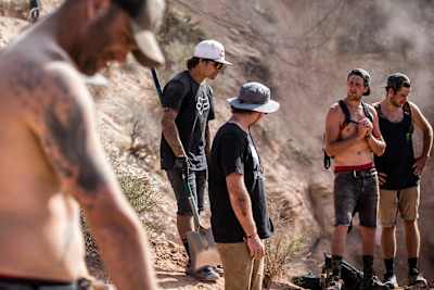 Two riders and their dig crews study lines up at a Red Bull Rampage mountain venue.