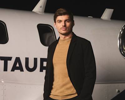 Max Verstappen vestindo roupas da AlphaTauri e em pé ao lado de um avião. 