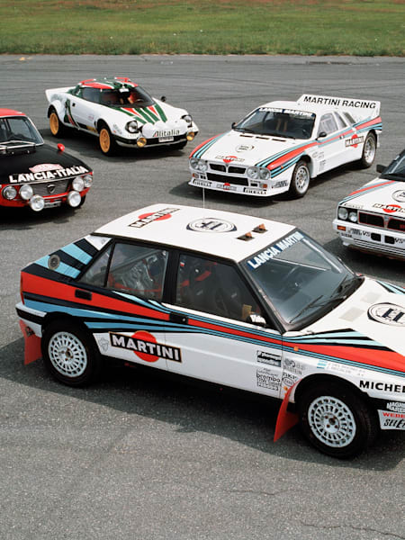 A Lancia Fulvia, an 037, a Stratos and two Deltas are displayed on the tarmac. 