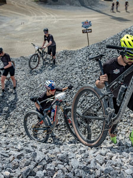 TeilnehmerInnen schieben bei Red Bull Radical im Steinbruch Ötelshofen ihre Bikes eine Steilpassage hoch.