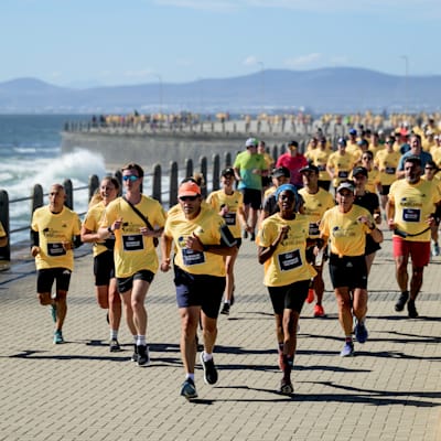 Participants wearing yellow World Run shirts run along the seafront promenade during the Wings for Life World Run App Run Event in Cape Town, South Africa, 2024