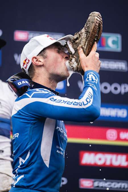 Ronan Dunne at the 2024 UCI Downhill World Cup in Loudenvielle-Peyragudes, France with the iconic muddy shoe toast on the podium