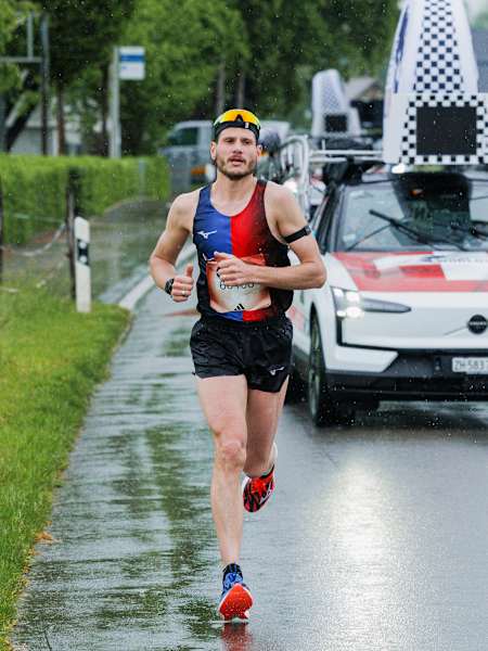Slovenian athlete Domen Hafner powers down a rainy street in Zug, Switzerland during the 2025 Wings for Life World Run with the Red Bull-branded Catcher Car close behind.