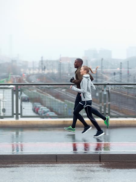 Para biegaczy biegnie kładką dla pieszych na tle miasta