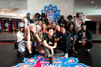 In 2024, a diverse group of top dancers from the Red Bull Dance Your Style competition pose backstage at the World Final event in Mumbai, India, with the iconic Red Bull logo prominently displayed