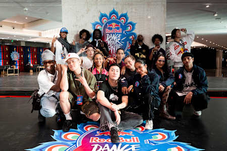 In 2024, a diverse group of top dancers from the Red Bull Dance Your Style competition pose backstage at the World Final event in Mumbai, India, with the iconic Red Bull logo prominently displayed