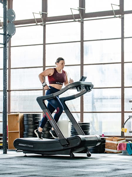 Pro fitness athlete Laura Horváth is running on a treadmill in a gym 