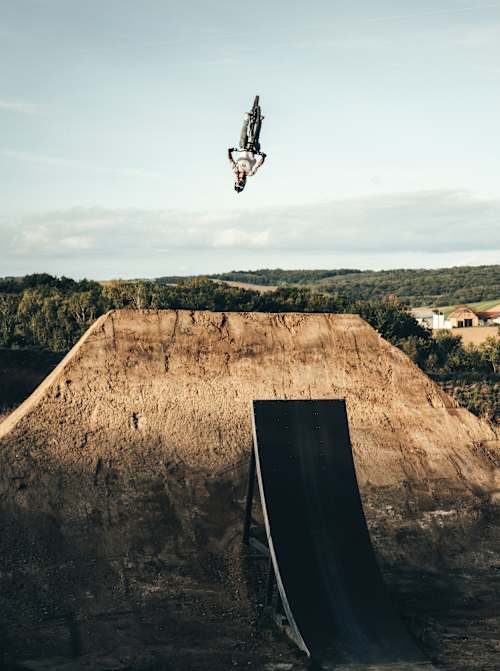 Austrian trials rider Fabio Wibmer does a trick off a ramp over a mound of earth.