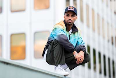 Majid is posing on a wall in front of a blurry building.