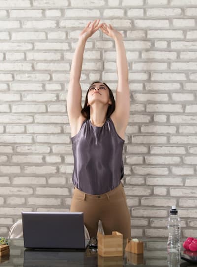 A woman stretches above her office desk.