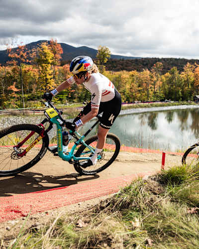 In 2024, Laura Stigger races her mountain bike amid vibrant fall foliage at the 2024 UCI XCO World Cup event in Lake Placid, USA