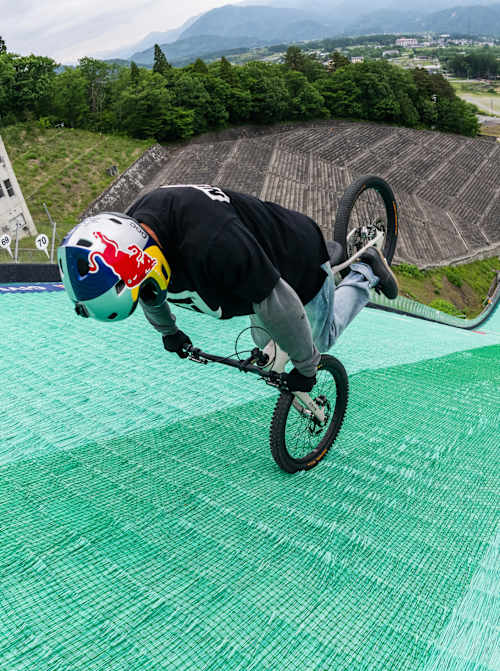 En mai 2026, Tomomi Nishikubo commence à dévaler un tremplin de saut à ski à Hakuba, au Japon, en roulant de dos.