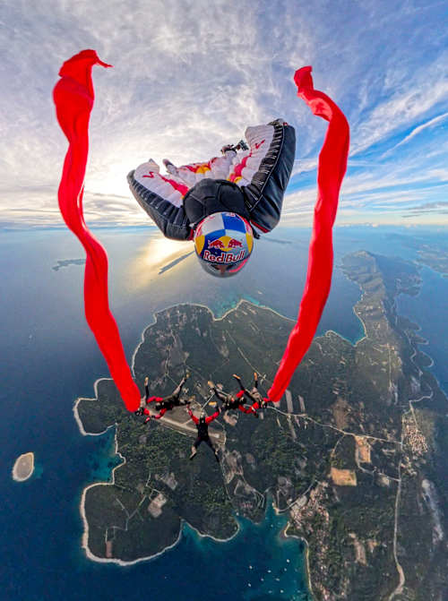 Andy Farrington soars over coastal Croatia in 2024, conquering the Red Bull Ultimate Aerial Obstacle Course with dramatic red streamers during an epic skydiving feat
