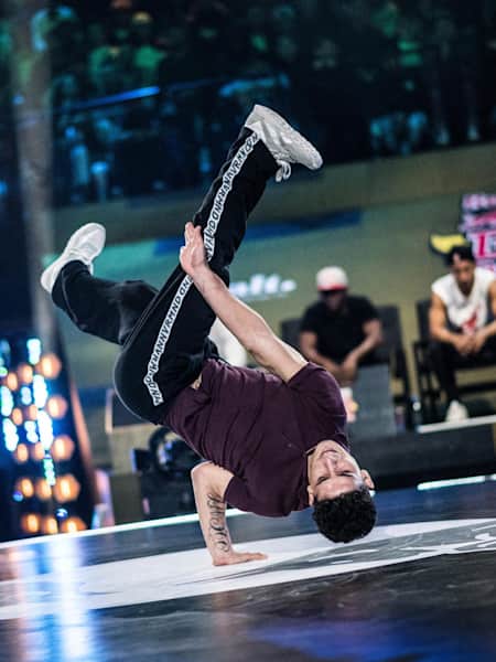 Lil Zoo resting on one hand upside-down at the Red Bull BC One World Final 2018. Judges are sitting in the background.
