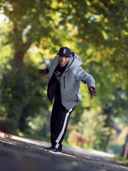 Tony GoGo dances on a street with trees in the background