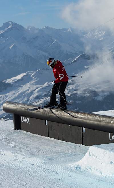 In 2023, Tess Ledeux performs at the Laax Open snowboarding event in Laax, Switzerland, showcasing her skills on a rail feature against a stunning mountain backdrop.