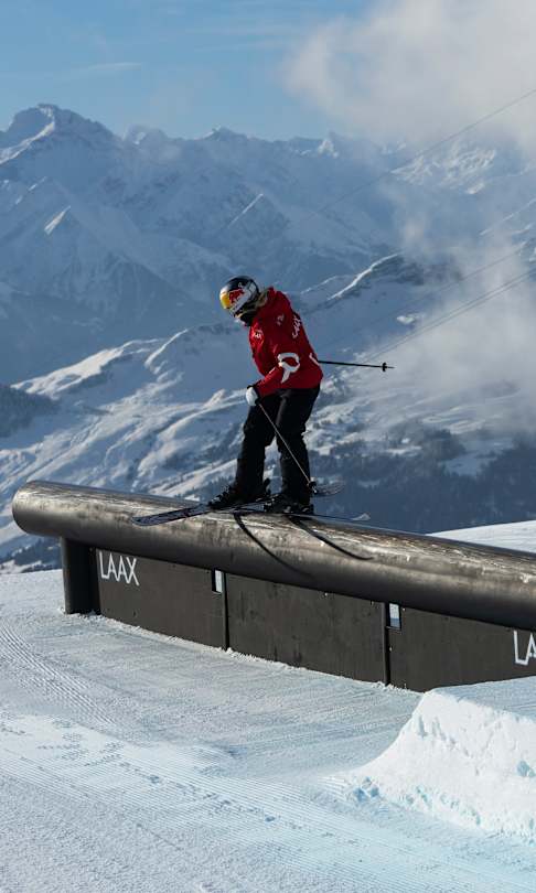 In 2023, Tess Ledeux performs at the Laax Open snowboarding event in Laax, Switzerland, showcasing her skills on a rail feature against a stunning mountain backdrop.