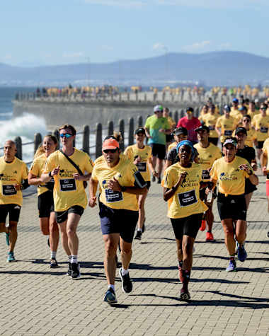 Participants wearing yellow World Run shirts run along the seafront promenade during the Wings for Life World Run App Run Event in Cape Town, South Africa, 2024