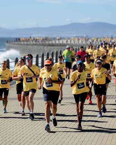 Participants wearing yellow World Run shirts run along the seafront promenade during the Wings for Life World Run App Run Event in Cape Town, South Africa, 2024