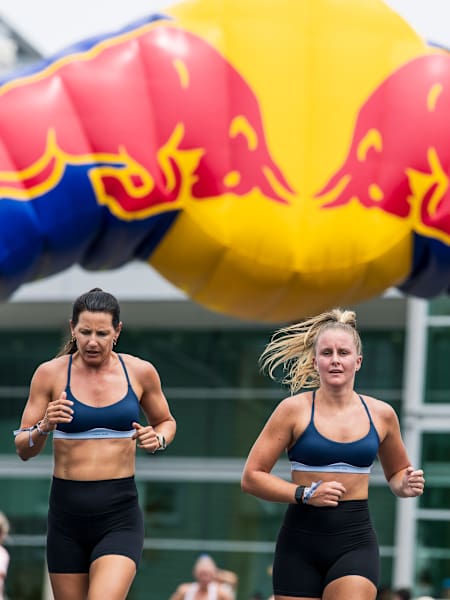 Deux athlètes féminines courent côte à côte sous une arche Red Bull lors d'une compétition HYROX.