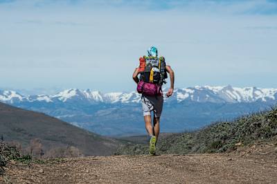 Race the Planet competitor runs with his kit on his back towards mountains.