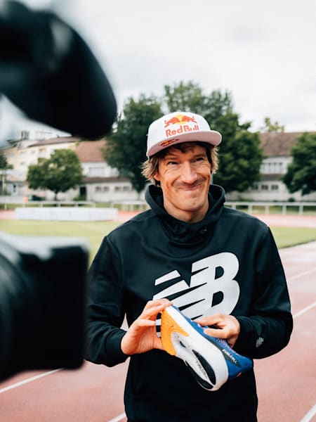 Triathlet Sebastian Kienle steht mit seinem New Balance Karbonplattenschuh vor einer Video-Kamera.