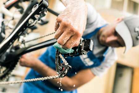 A mechanic cleans the rear derailleur on a bicycle.