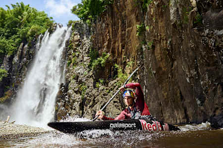 Un kayakiste pagaie dans une rivière près d'une chute.