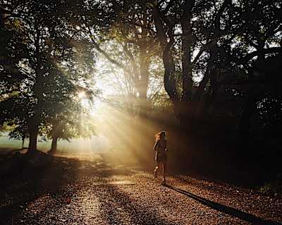 Eine Frau läuft in der Morgensonne durch einen Park im englischen Hampstead Heath.
