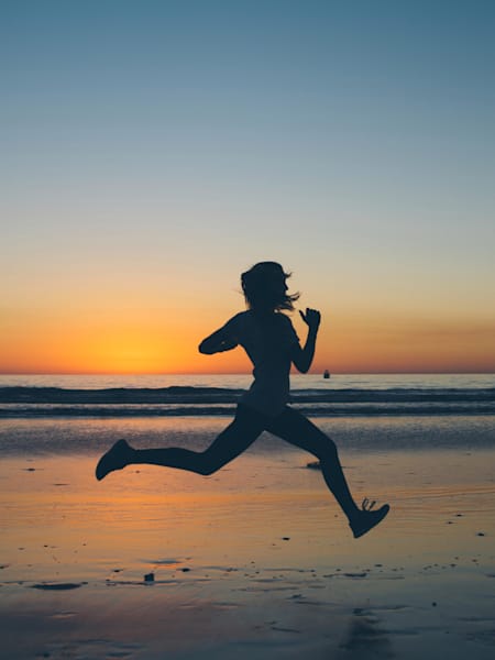 A silhouetted runner jogs along beach at sunset.