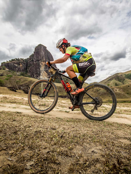 Mountain biker rides up hill with mountain backdrop.