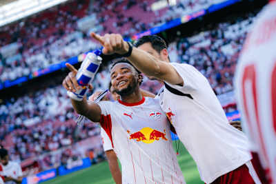 Christopher Nkunku nach dem 3:0-Erfolg von RB Leipzig gegen Borussia Mönchengladbach grinsend mit Red Bull-Flasche.