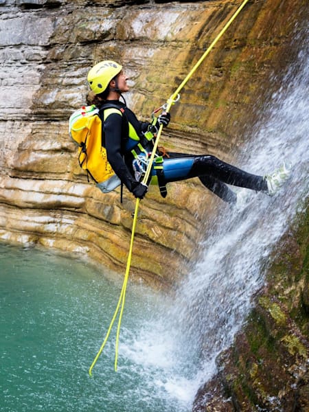 An adventurer goes down a small waterfall while Canyoning in a remote location.