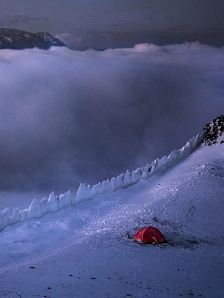 Tent on the edge of a snowy ledge high up in the mountains.
