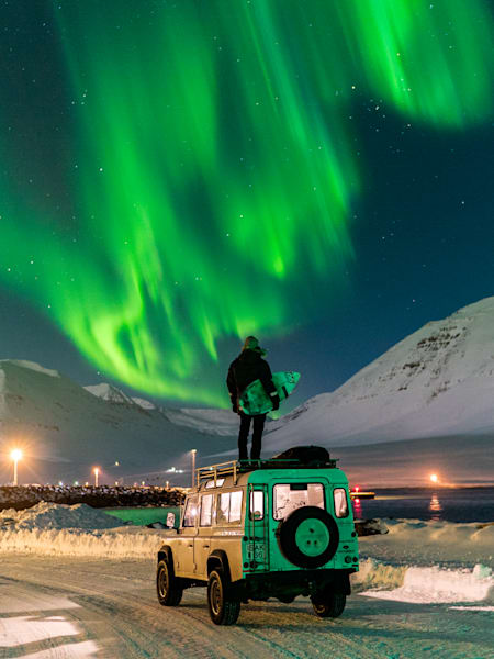 Profesjonalny surfer z Islandii Heidar Logi na dachu swojego samochodu. W tle zorza polarna.