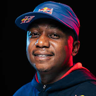 In 2024, Samkeliso Thubane smiles brightly while wearing Red Bull branded apparel against a dark background in Johannesburg, South Africa.